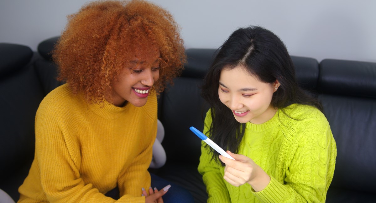 Two women smiling and looking at positive pregnancy test