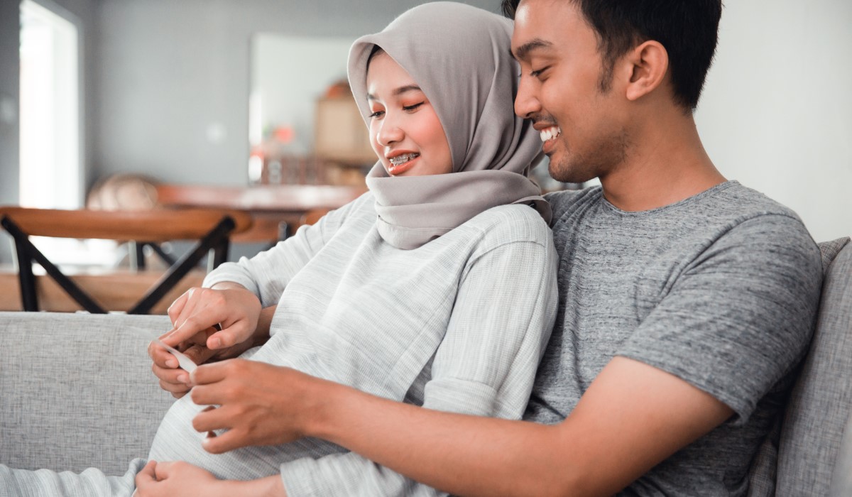 Pregnant woman leaning back against her partner, both smiling and looking at an ultrasound picture