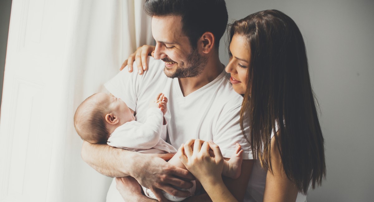 Father holding newborn with mother by his side