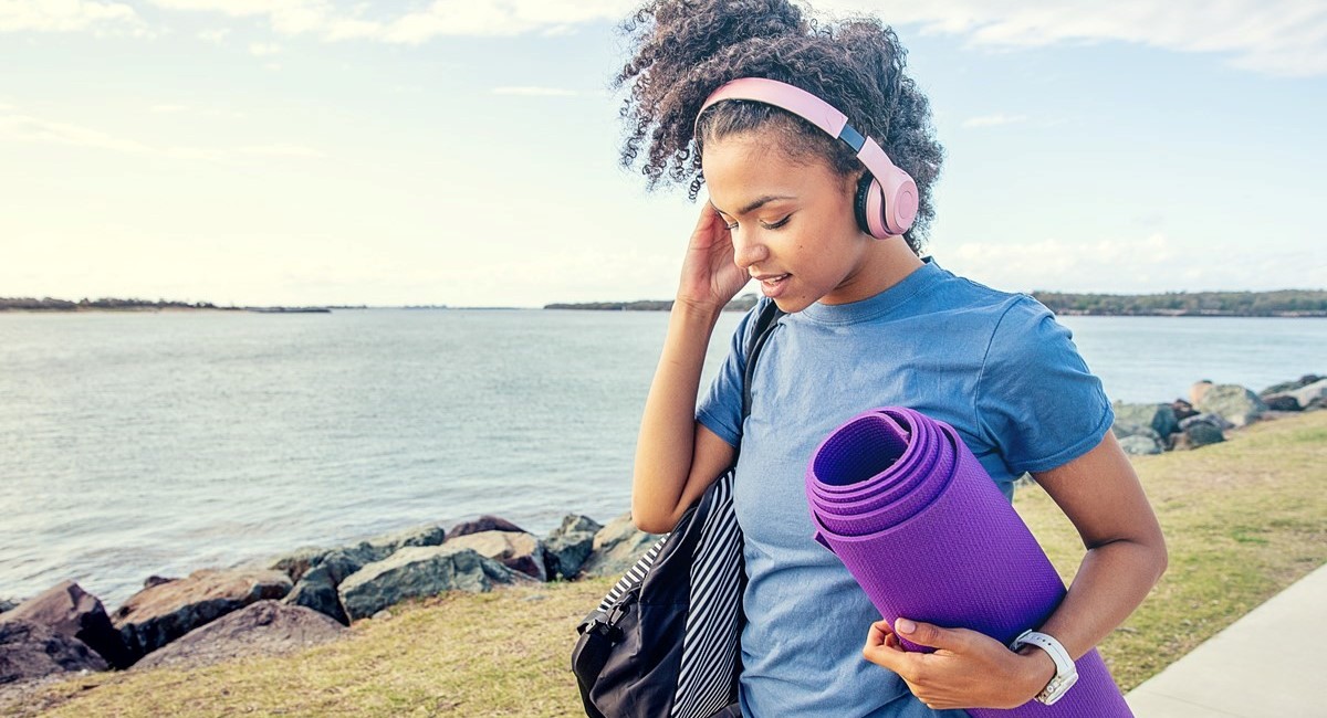 Woman carrying yoga mat listening to music through headphones