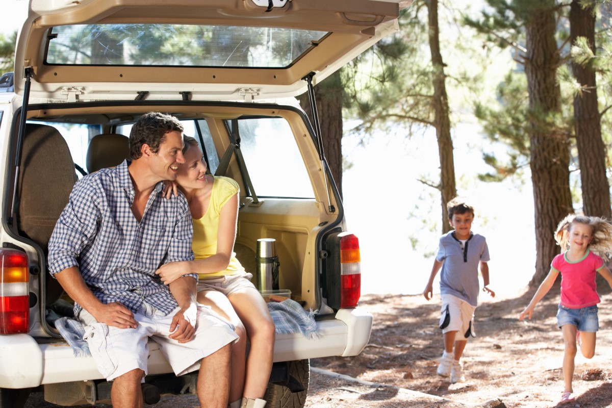 Man and woman sitting in the back of a 4WD, with happy kids on the sand next to them at the beach
