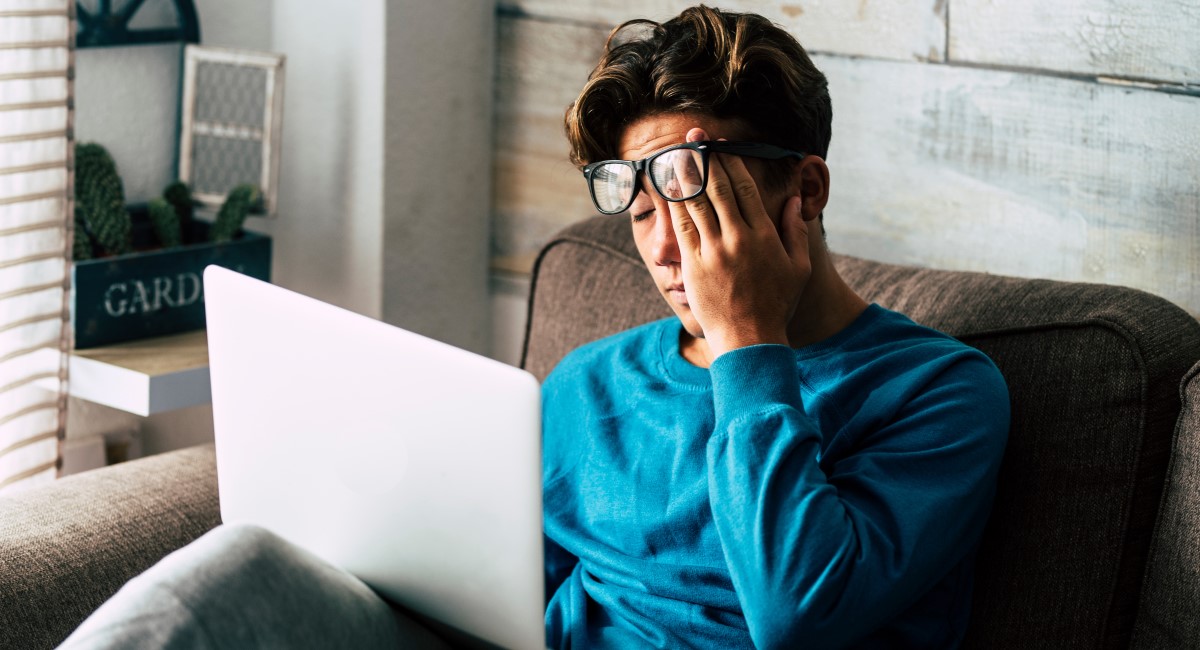 Man rubbing his face while looking at laptop