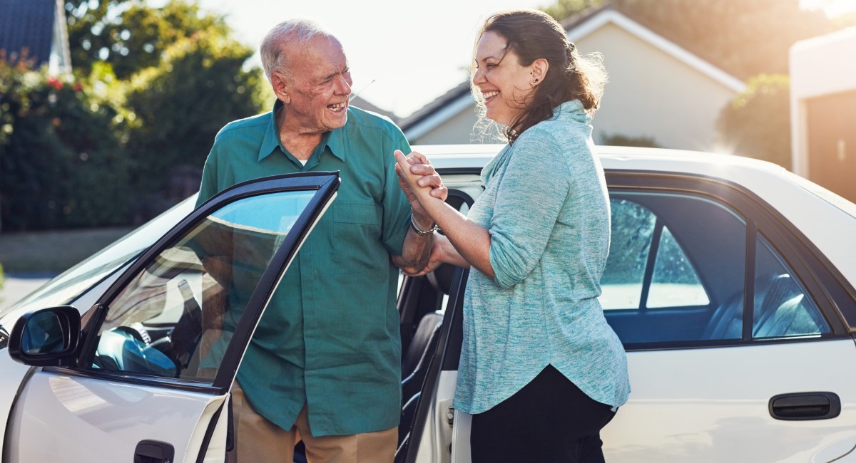 Woman helping elderly man into a car