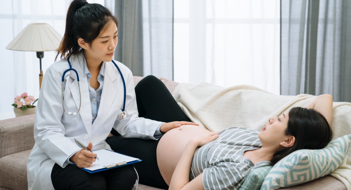 Pregnant woman lying on couch being examined by doctor