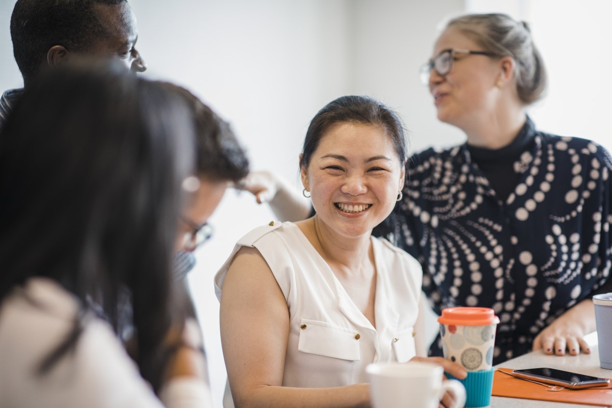 Smiling woman enjoying a cup of coffee with workmates