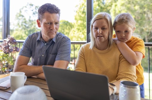Man and woman looking at laptop screen, young daughter looking over woman's shoulder