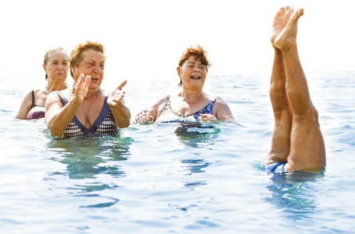 Older women in swimming doing water aerobics. One person is upside down with legs sticking out of the water.