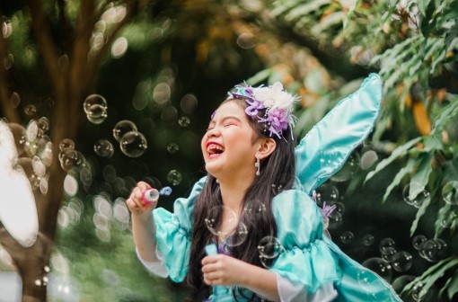 Young girl in fairy costume laughing and blowing bubbles
