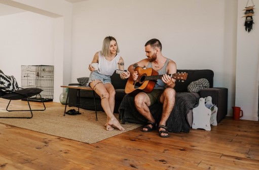 Young man strumming guitar on couch, woman sitting next to him