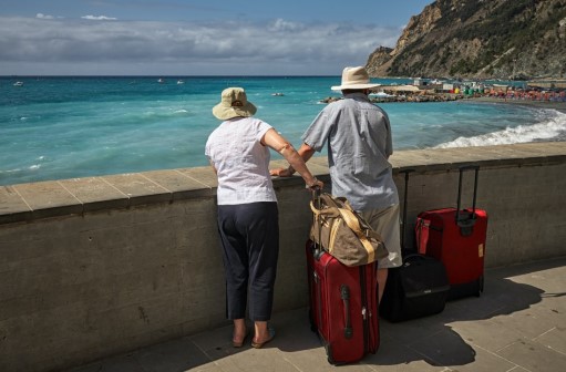 Older man and woman with suitcases looking out over a beach 