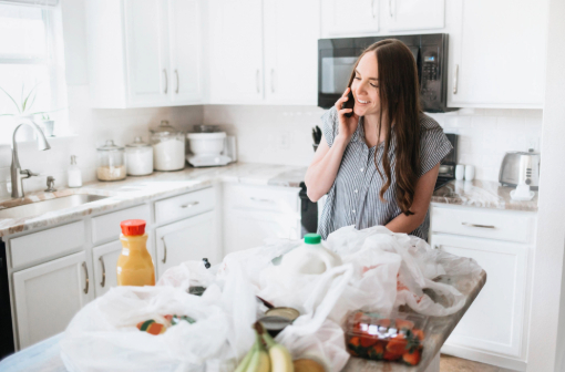 A woman on the phone while standing over a table of groceries
