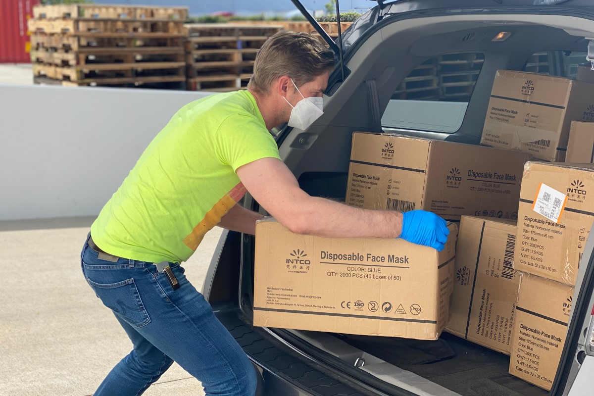 Man volunteering, lifting boxes of face masks out of a car