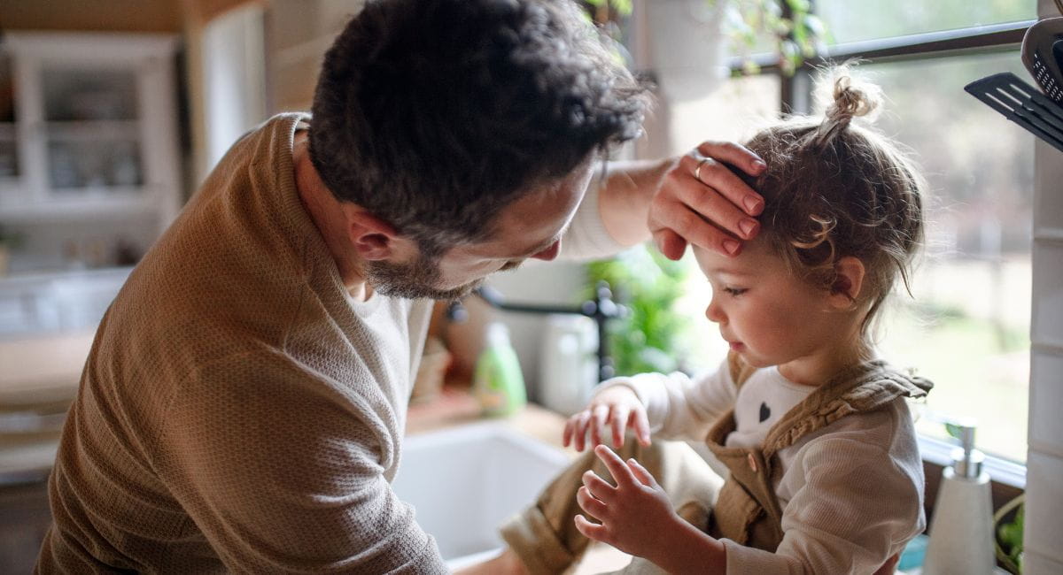 A man holding his hand to a young child's forehead