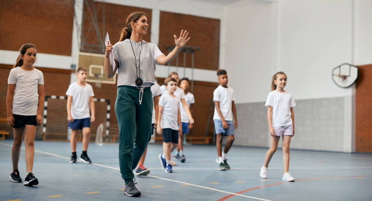 A woman walking on a basketball court while coaching a group of children