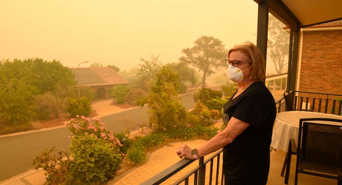 A woman standing on a balcony wearing a mask overlooking a smoky street
