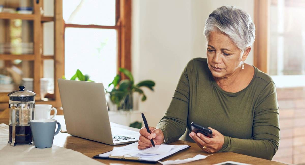 A senior woman sitting at a kitchen table while writing on a piece of paper