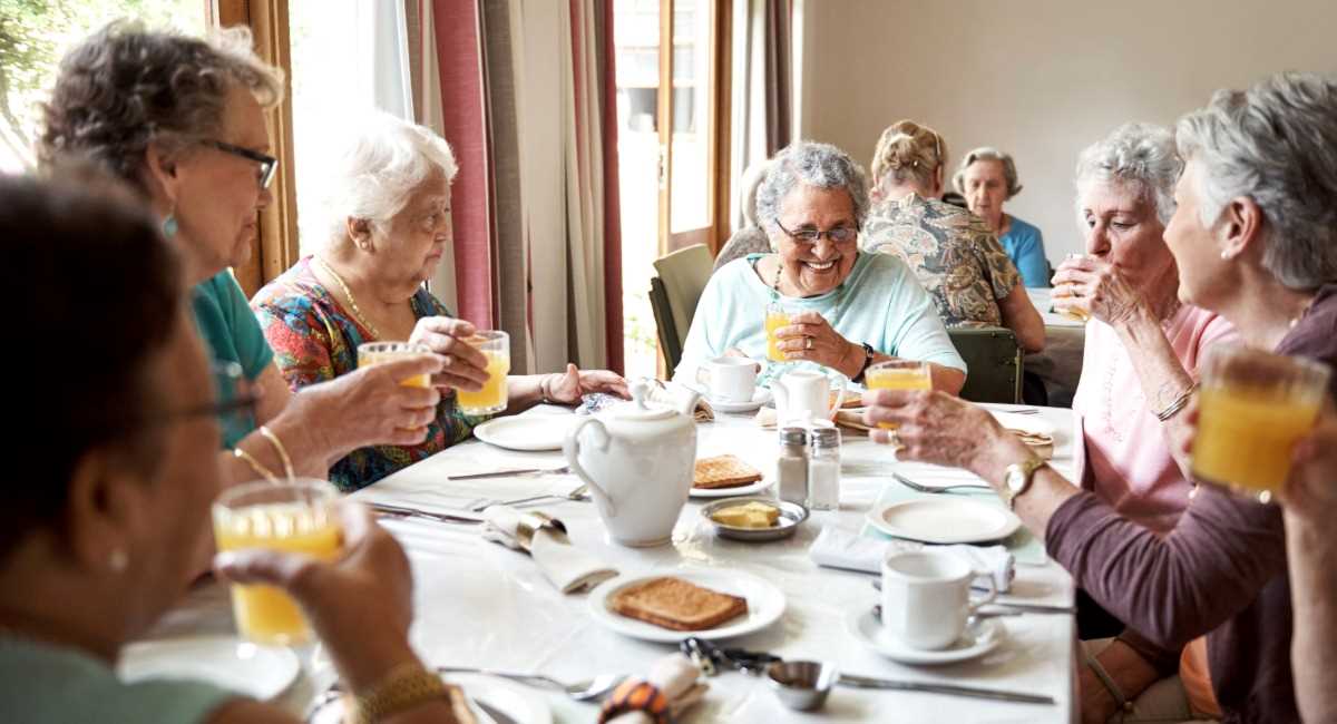 A group of seniors enjoying each other's company while sipping orange juice at breakfast