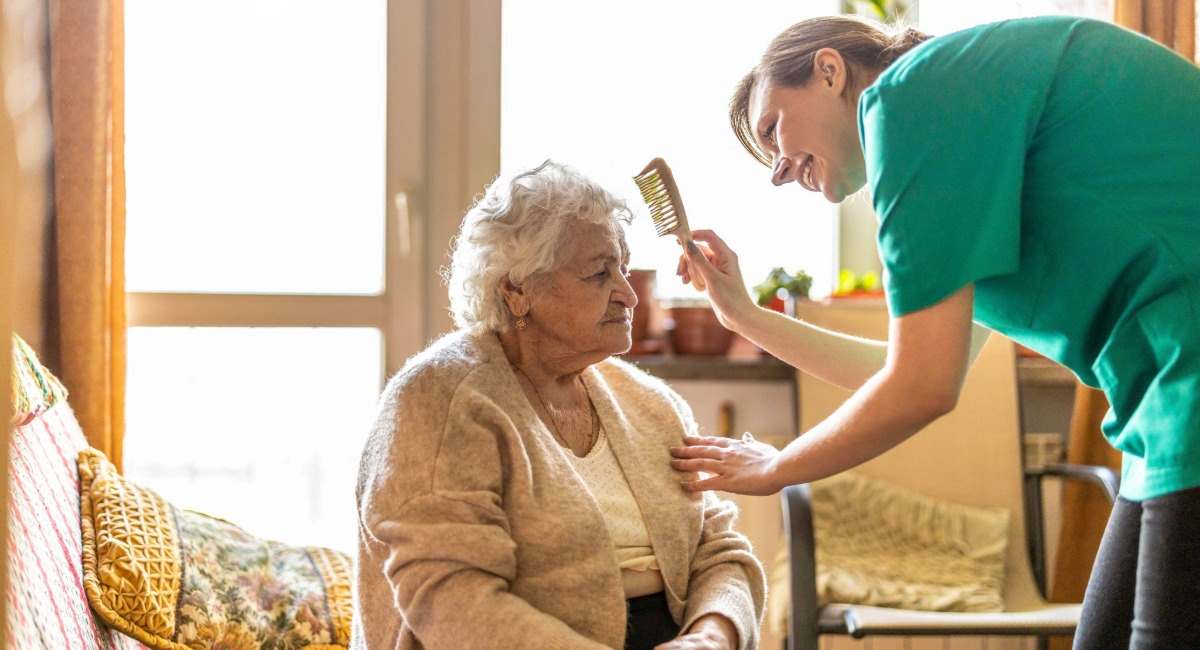 An elderly woman having her hair brushed by a care worker
