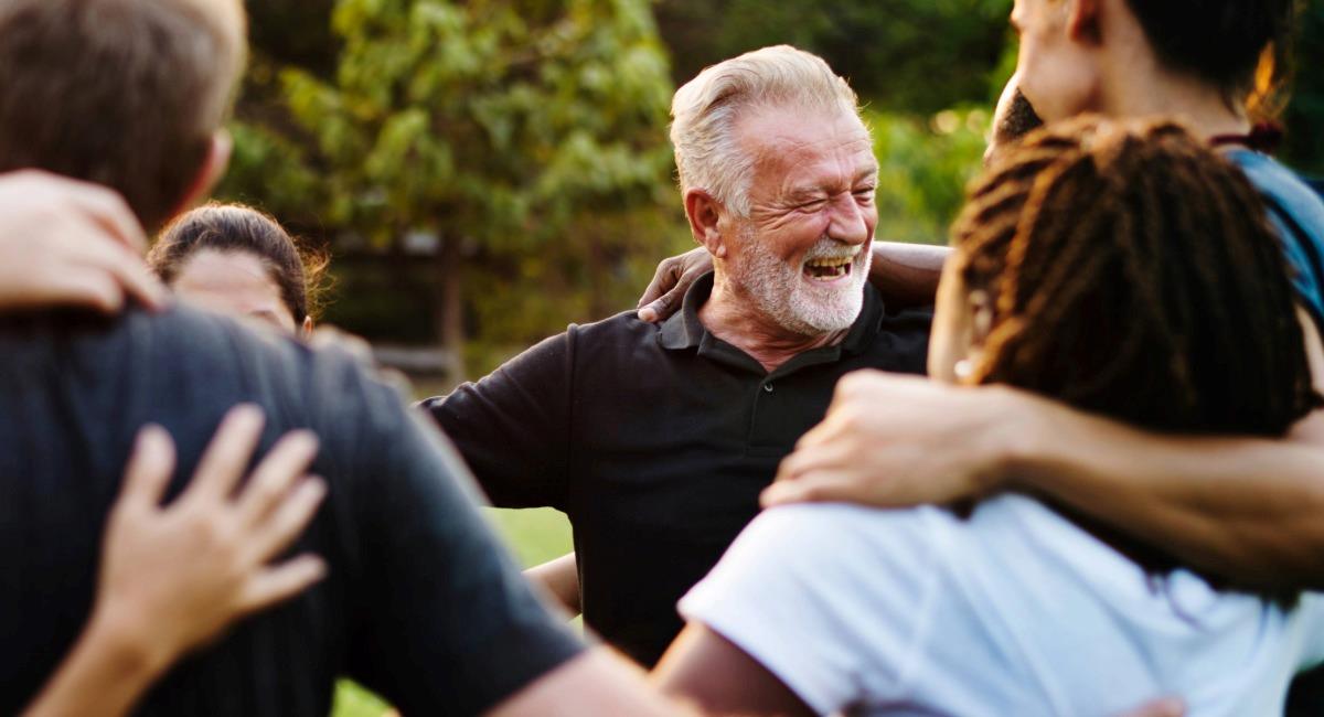 A man smiling while standing within a group of people in an embrace
