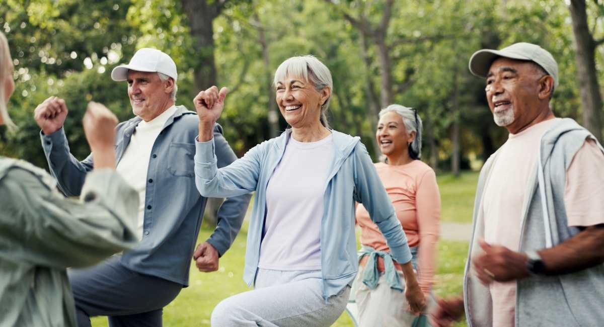 A group of people wearing exercise gear smiling while taking part in an exercise class at a park