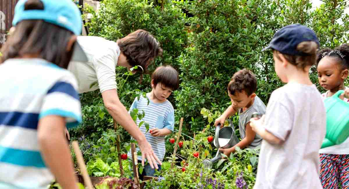 A woman pointing to a plant in a vegetable garden while surrounded by a small group of children