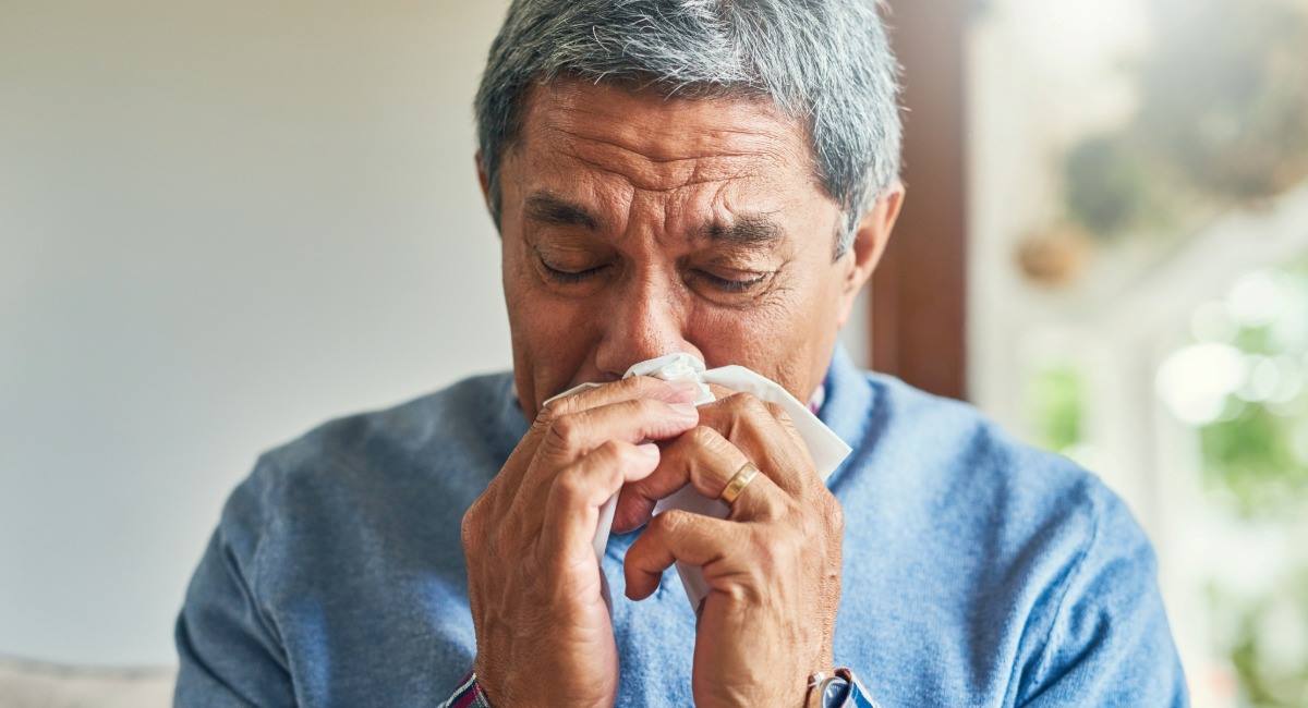 A senior man wearing a blue shirt blowing his nose