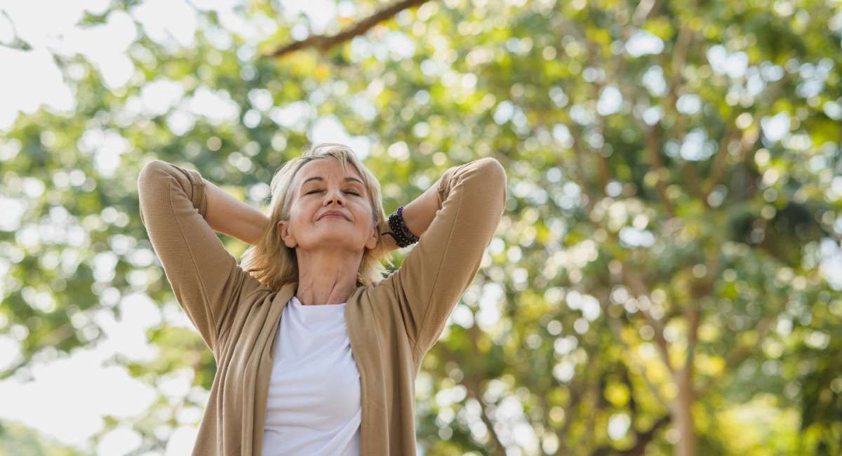 A woman happily breathing easily outside among trees