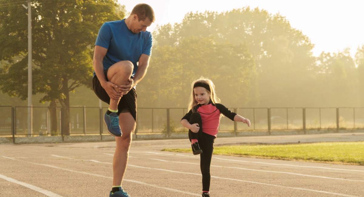 A man and his young daughter stretching on a running track