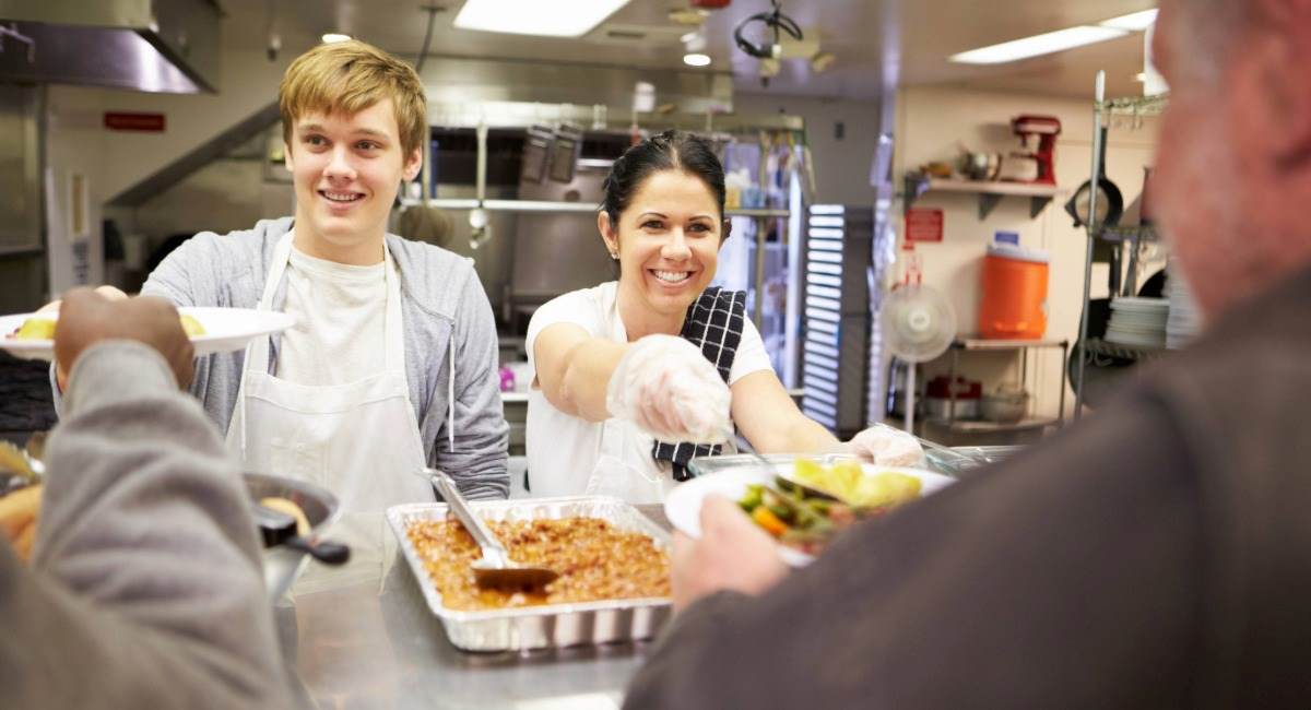 Two volunteers in a kitchen serving food to people