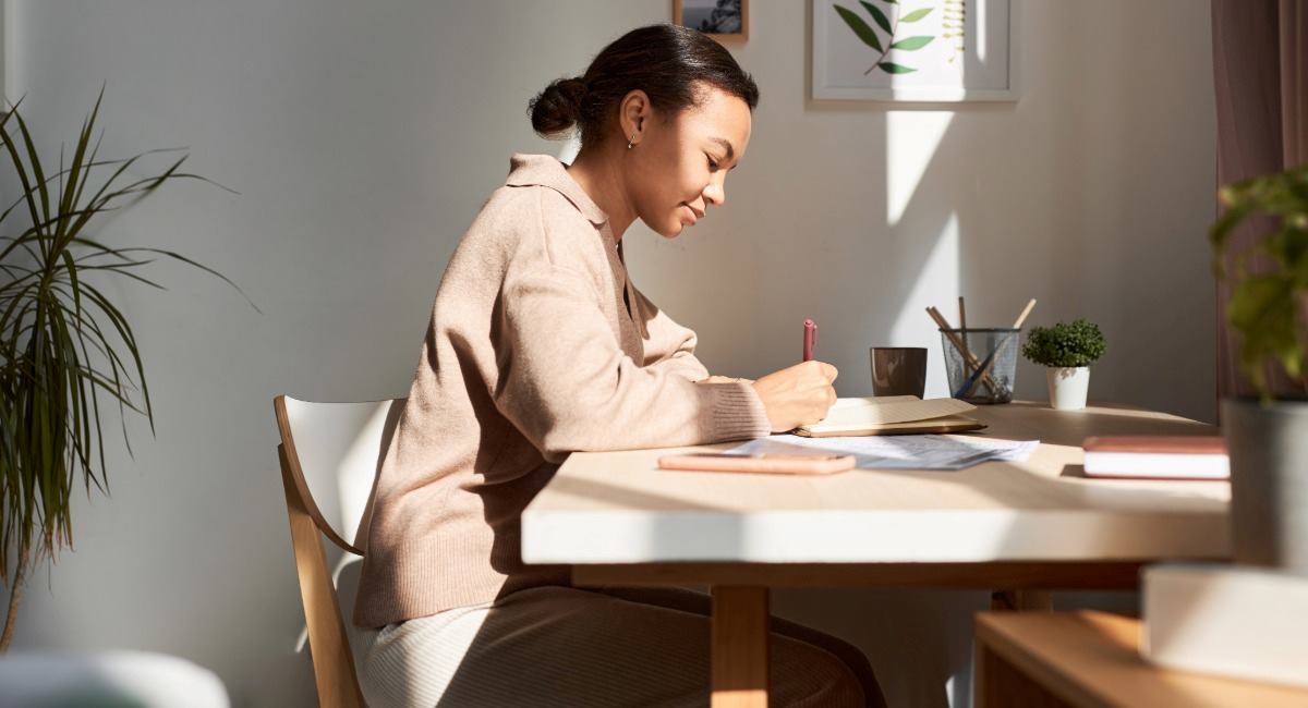 A young woman sitting at a table writing in a notebook