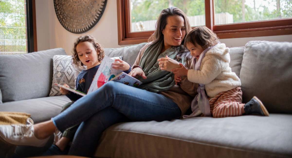 A woman sitting on a couch while playing with her two young daughters