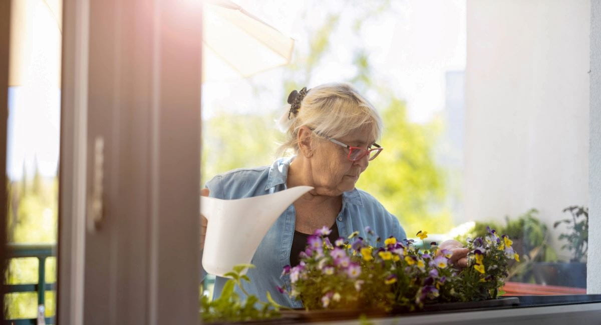 A woman holding a watering can while tending to flowers on a balcony
