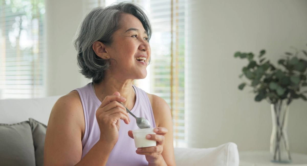 A middle-aged woman wearing activewear sitting on a couch eating yoghurt
