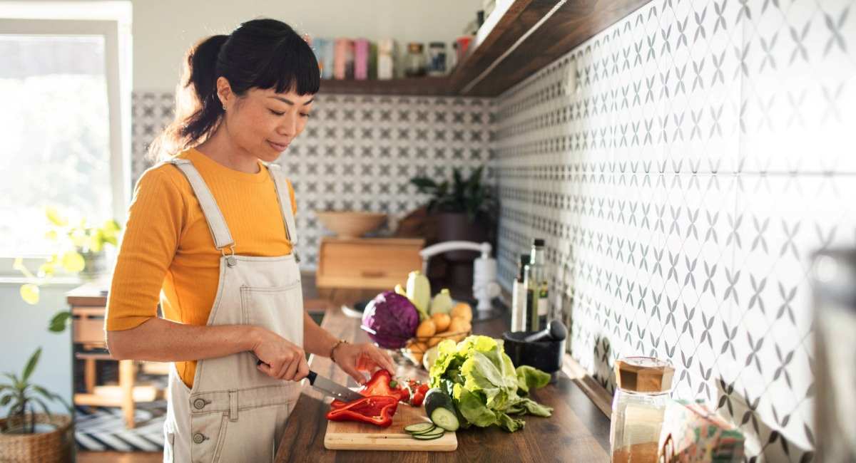 A young woman wearing an apron chopping vegetables in a kitchen