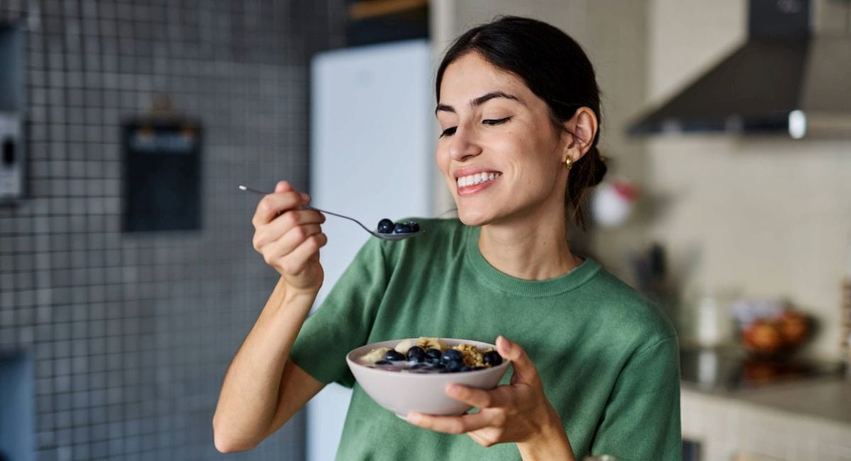 A woman smiling while holding a bowl of fruit and muesli
