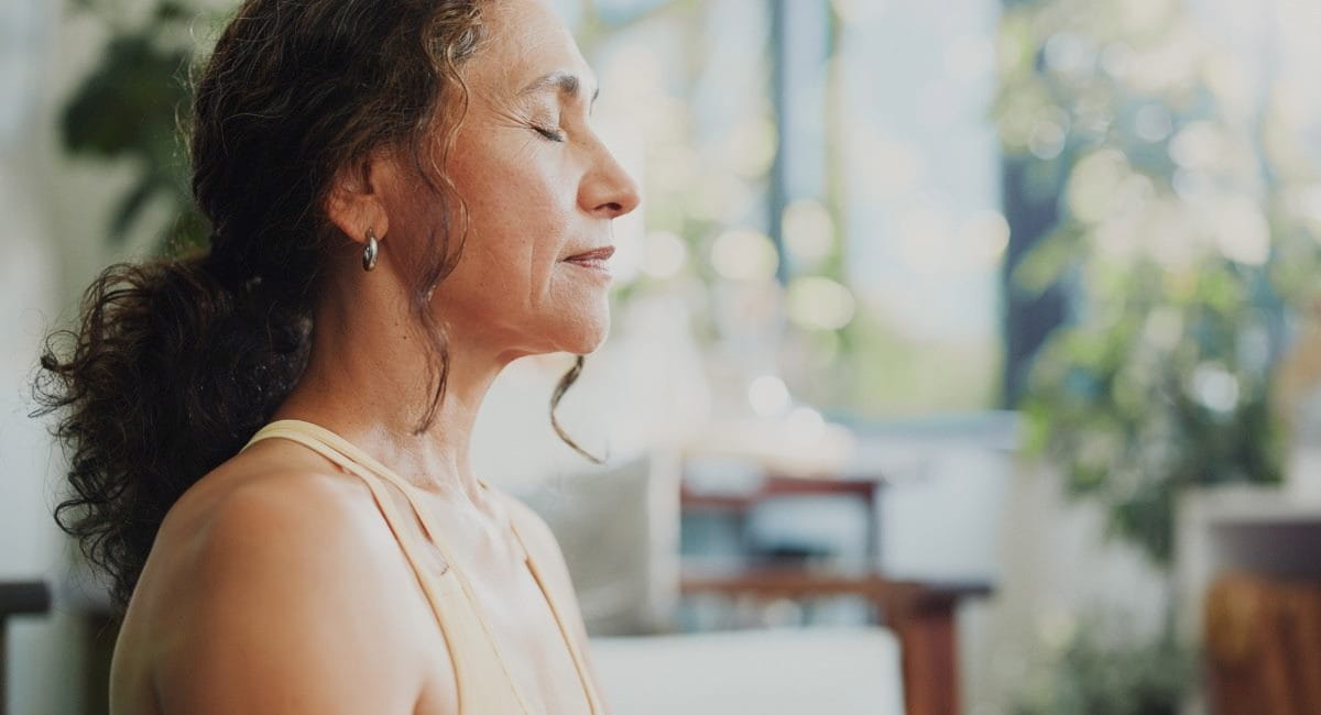 A middle-aged woman peacefully meditating at home while wearing exercise attire