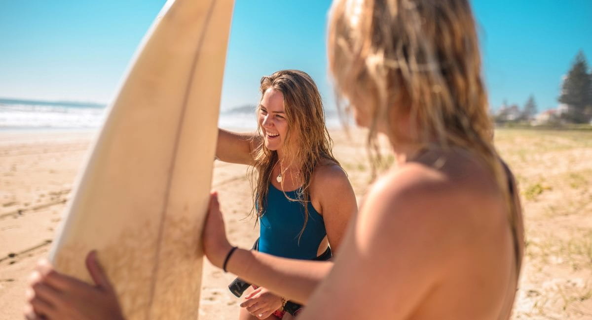 Two young women laughing at the beach while holding surfboards