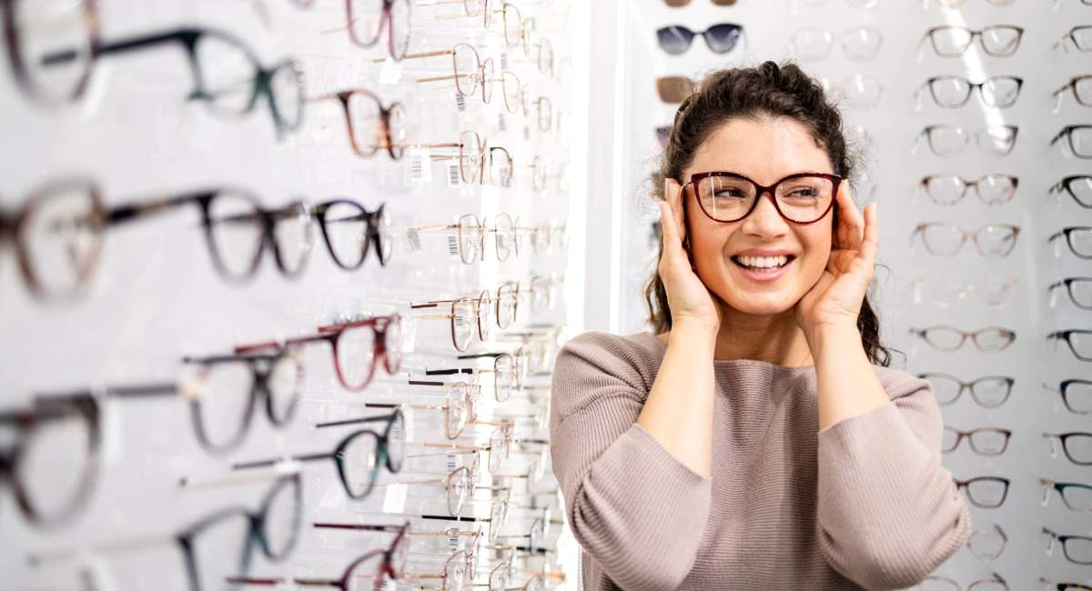 A woman smiling while trying on glasses in a glasses store