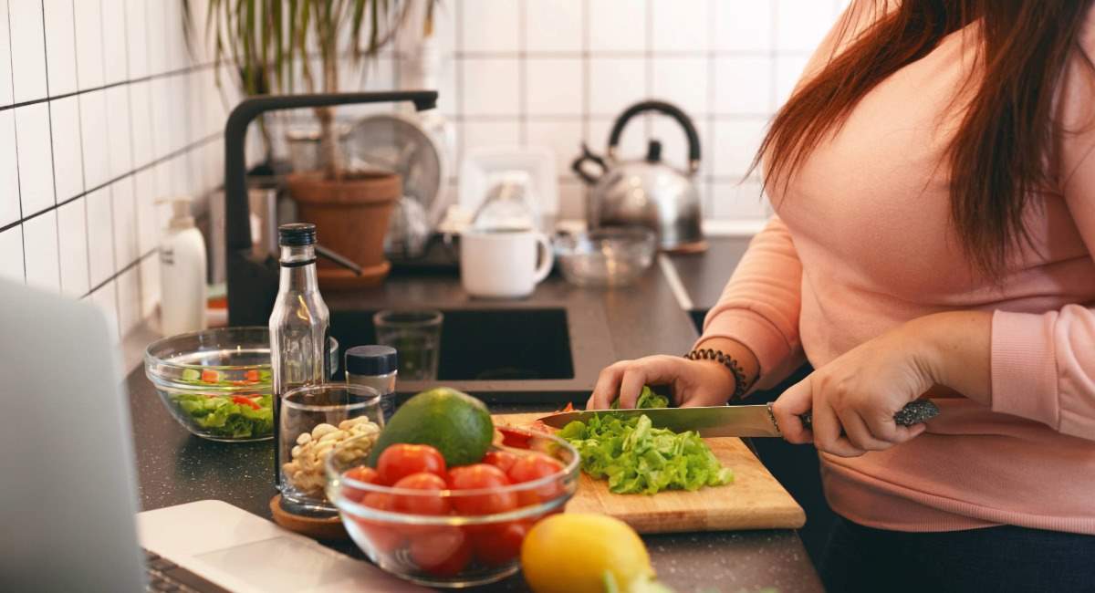 A woman cutting lettuce on a kitchen bench surrounded by other fresh fruit and vegetables