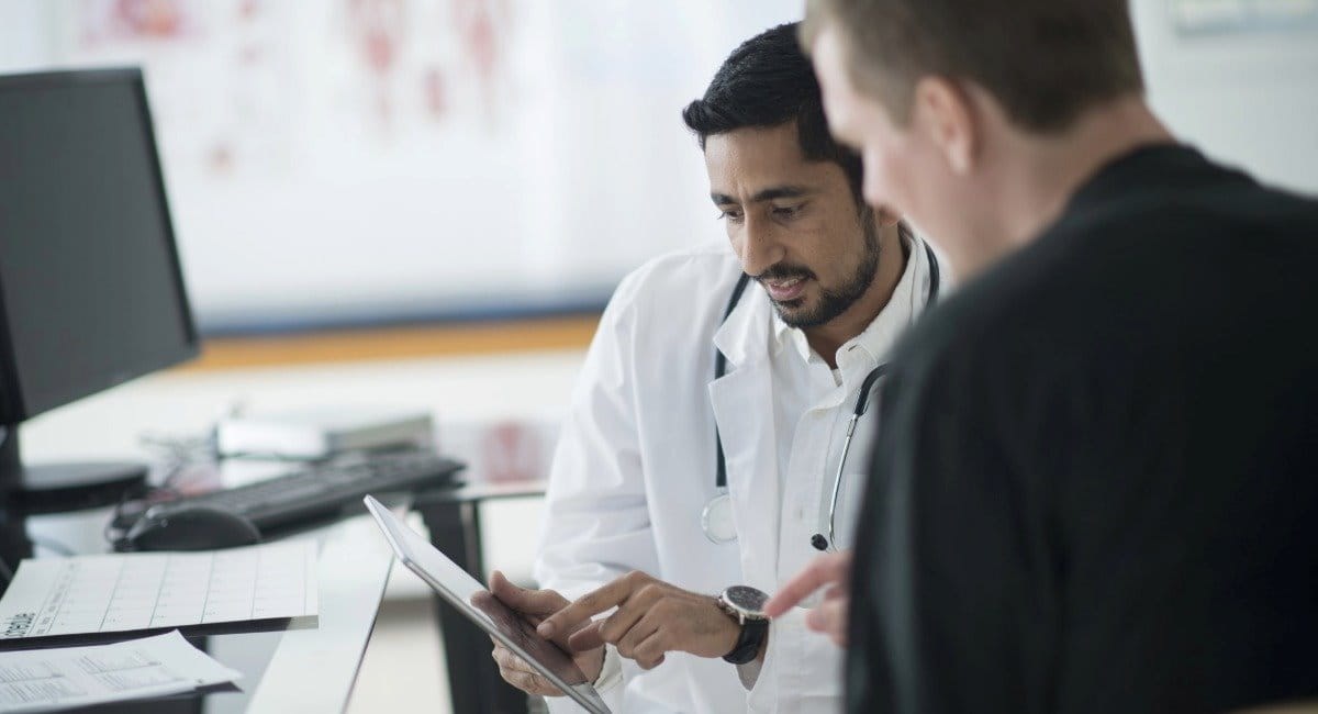 A doctor pointing at a screen while talking to a middle aged man