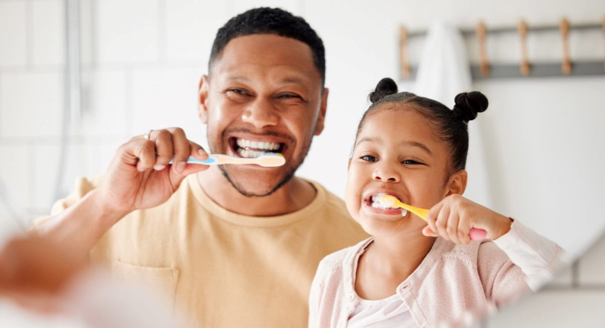 A father and young daughter brushing their teeth together in the bathroom
