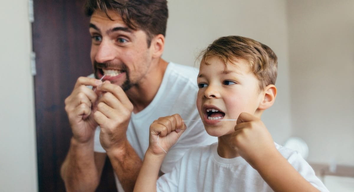 A father and son flossing their teeth together in the bathroom