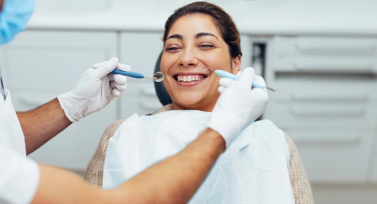 A woman smiling while sitting in a dental chair receiving dental treatment