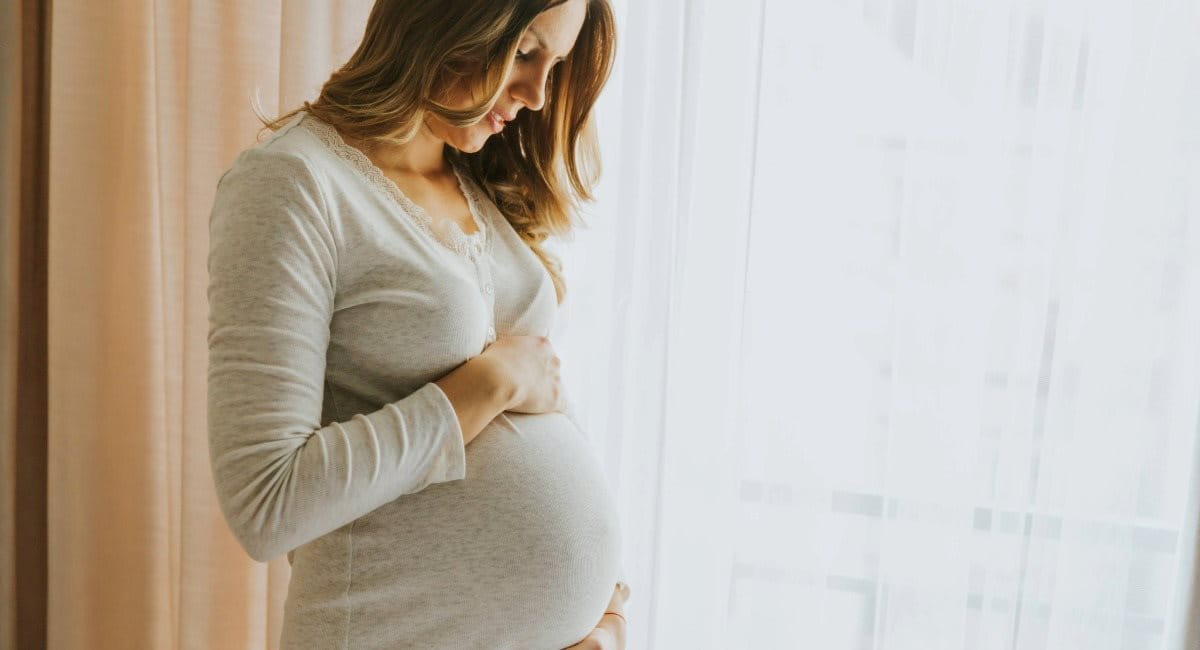 A woman looking down while holding her pregnant belly