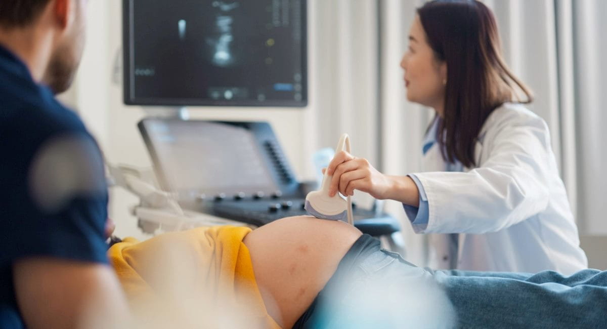 A pregnant woman receiving an ultrasound from a doctor with a man sitting next to her
