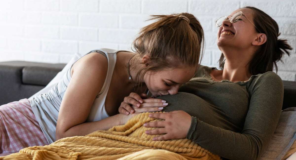 A woman kissing the belly of a pregnant woman who is smiling