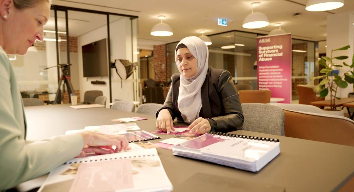Two women sitting at a desk in an office looking at Arise paperwork