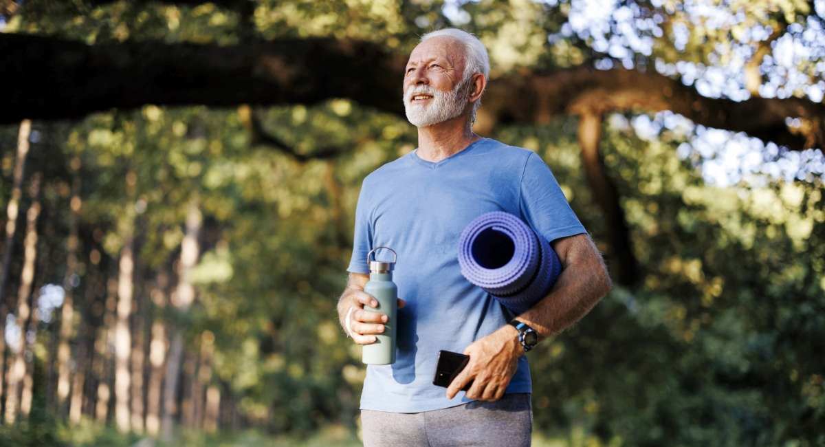 A senior male holding a yoga mat and water bottle
