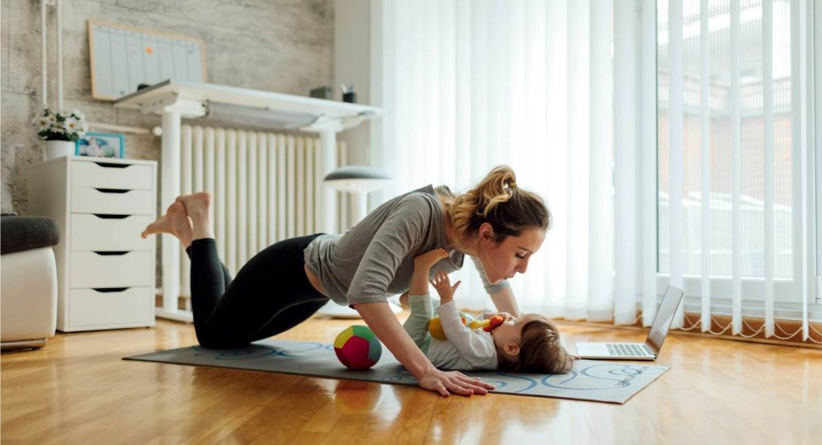 A mother doing a push up on a yoga mat where a toddler is laying