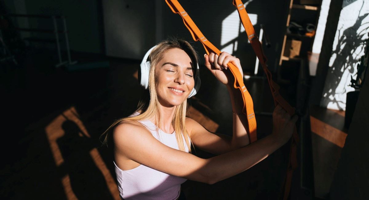 A young woman smiling while wearing headphones and using gym equipment